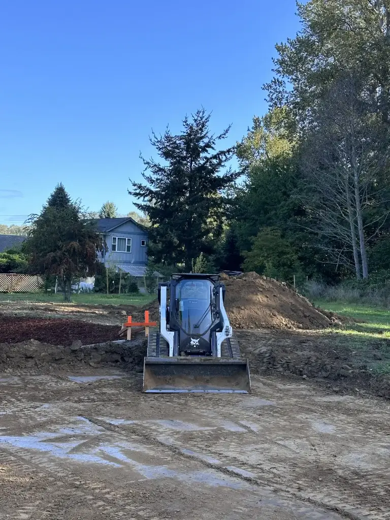 Home 13 Residential foundation dig with excavator, A commercial excavator executing professional digging services to clear brush, level terrain, and prepare a stable foundation for a new building.